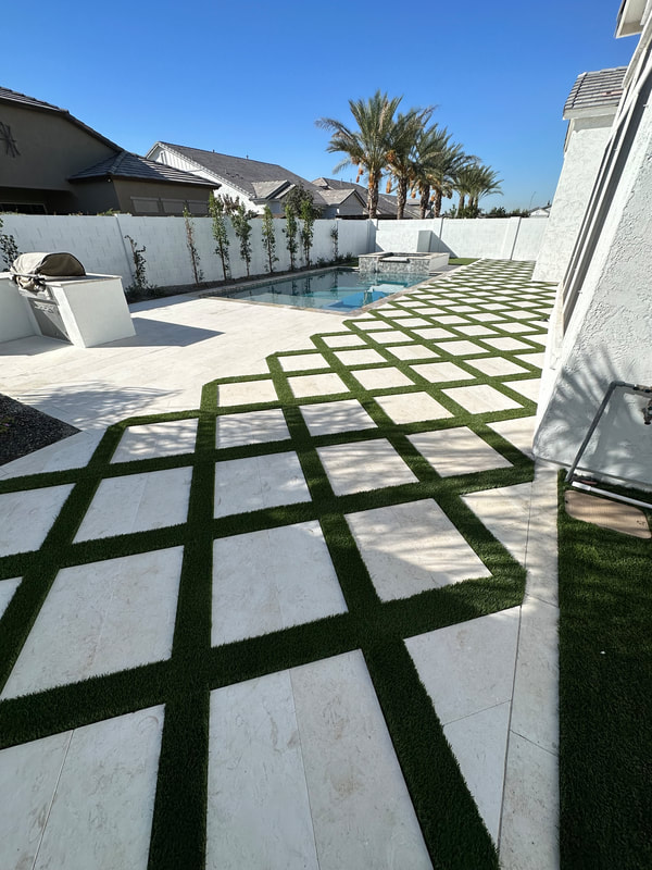 Cream-colored travertine tiles line the poolside area, complemented by lounge chairs and lush landscaping, creating a relaxing outdoor oasis